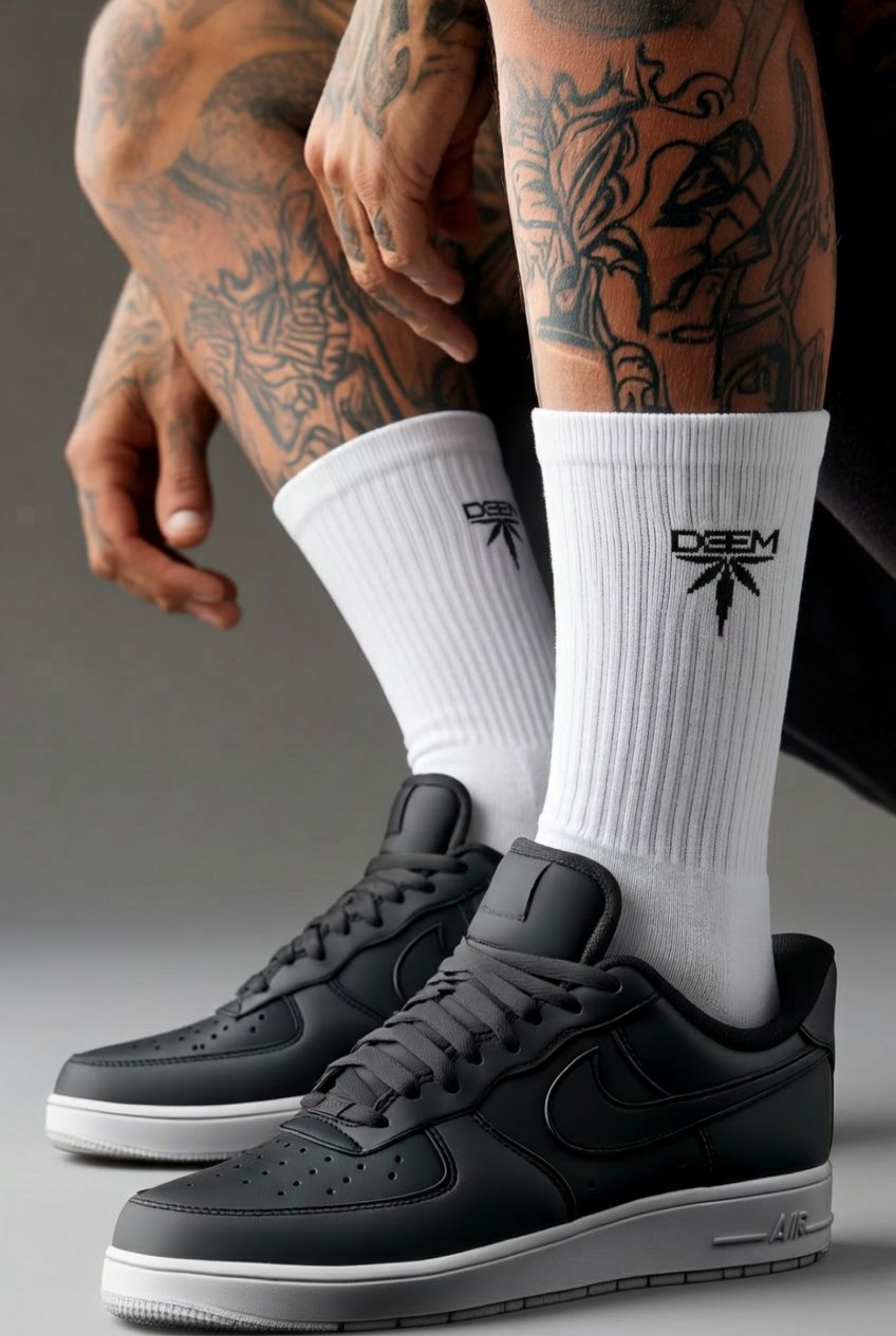 Person wearing black sneakers and white socks with a logo, sitting on a dark surface.