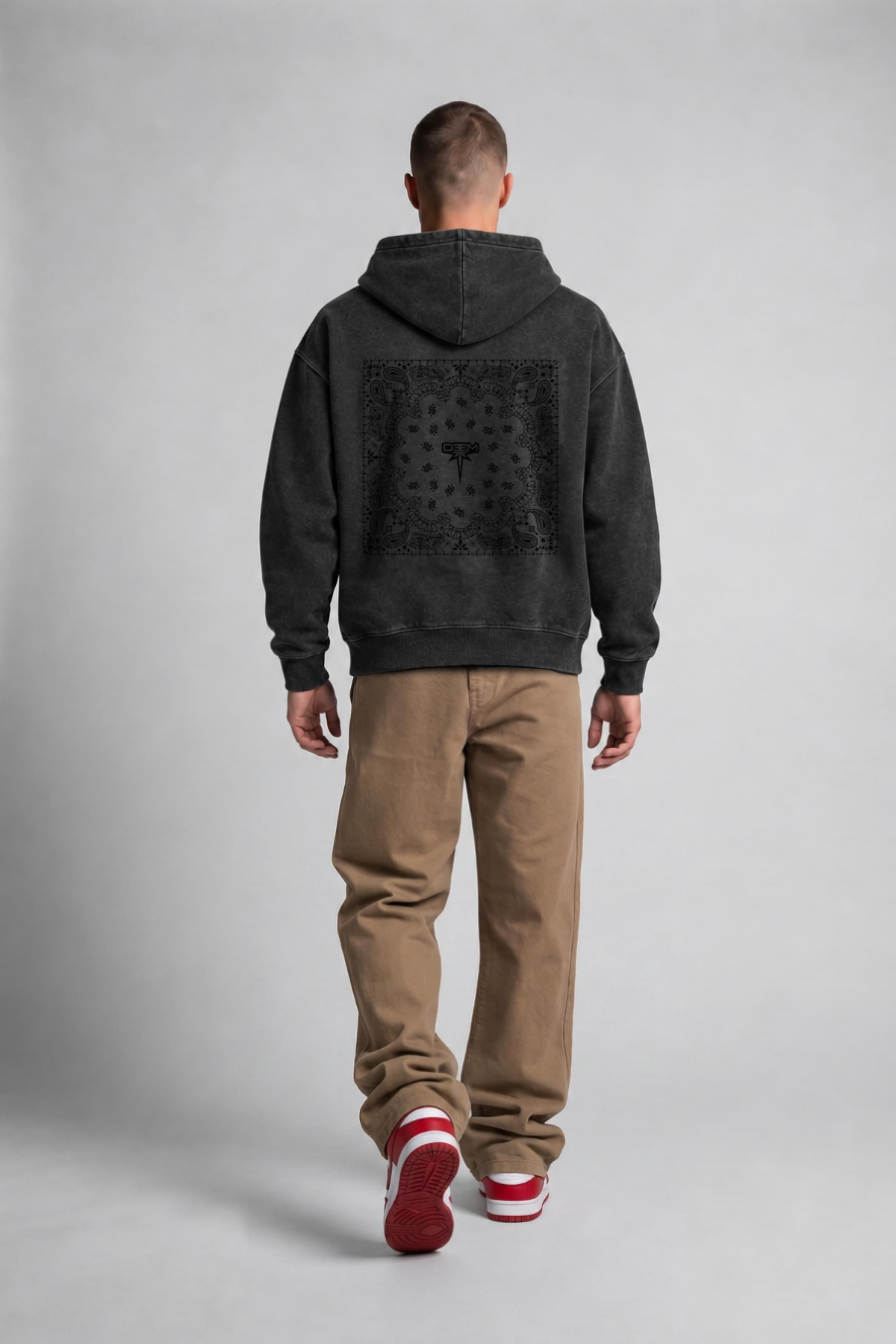 Model wearing the Bandana Vintage Hoodie in garment-dyed black, back view with tonal bandana print and DEEM sygnet