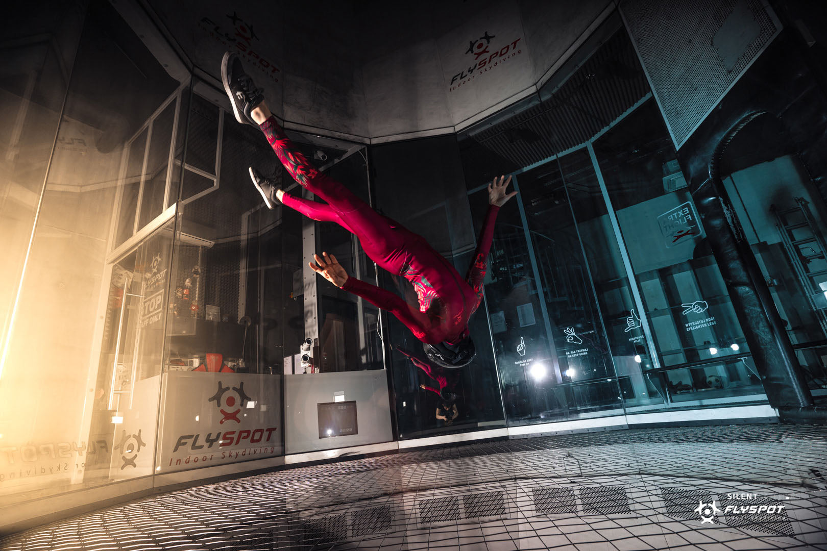 Person in a red jumpsuit free falling inside an indoor skydiving facility.